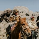 Mongolscy myśliwi na koniach z orłami przednimi na skalistym pustkowiu
